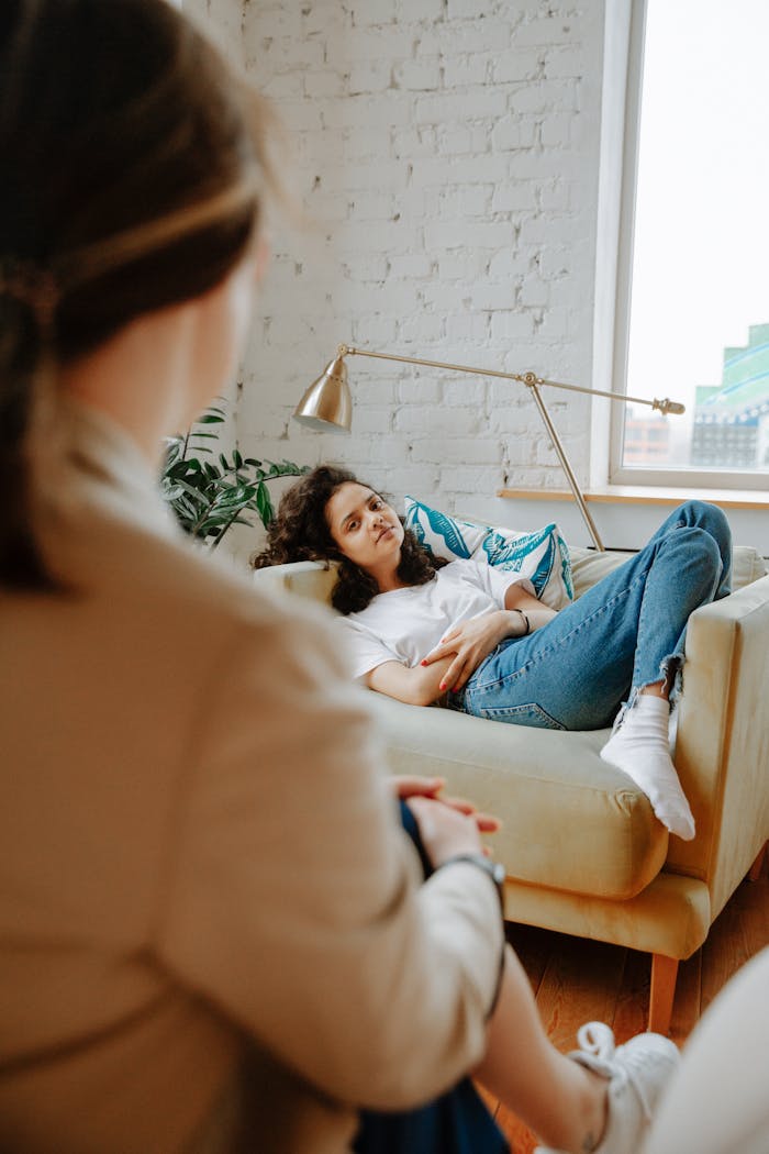 A young woman in a casual therapy session, relaxing on a sofa, while a therapist listens attentively.